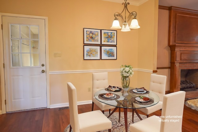 dining area featuring ornamental molding, a notable chandelier, a fireplace, and dark hardwood / wood-style flooring