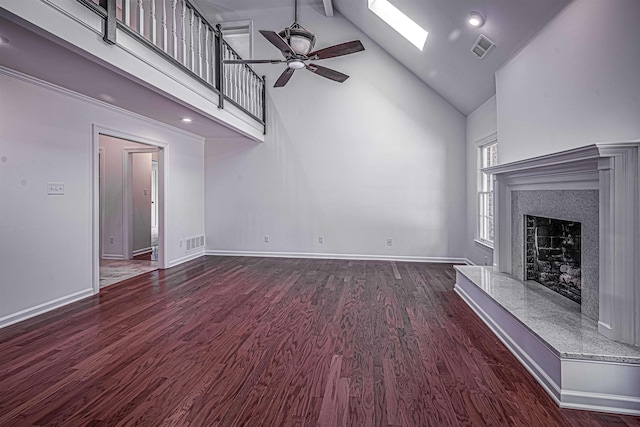 unfurnished living room featuring beam ceiling, high vaulted ceiling, dark hardwood / wood-style floors, a fireplace, and a skylight