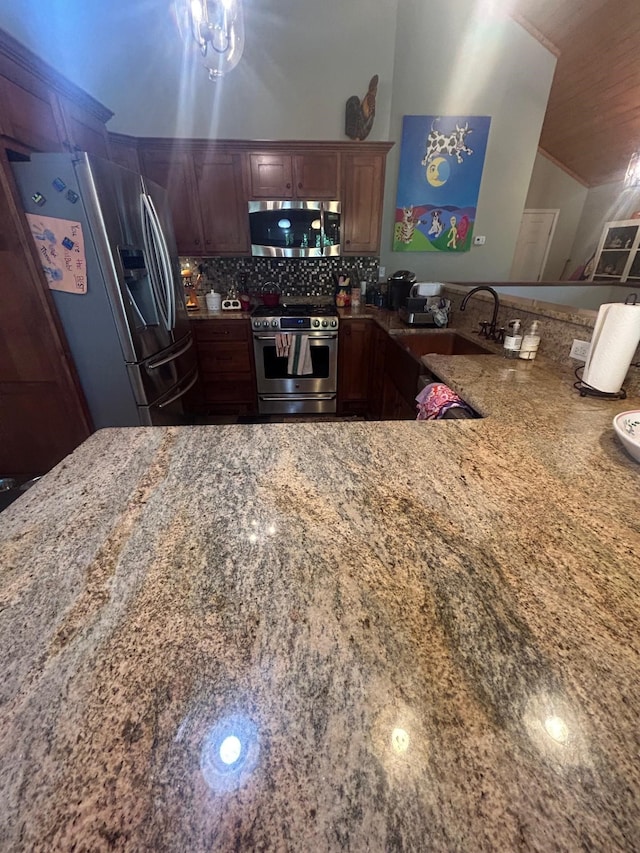 kitchen with kitchen peninsula, sink, appliances with stainless steel finishes, light stone counters, and tasteful backsplash