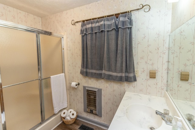 bathroom with vanity, a textured ceiling, heating unit, and an enclosed shower