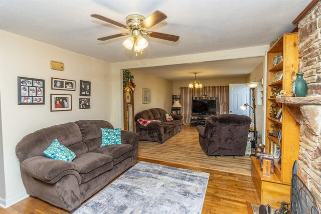 living room with a textured ceiling, a fireplace, ceiling fan with notable chandelier, and light hardwood / wood-style floors