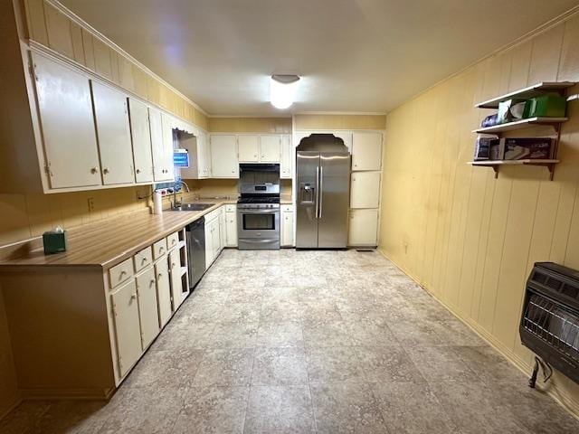 kitchen featuring heating unit, appliances with stainless steel finishes, white cabinetry, wood walls, and sink