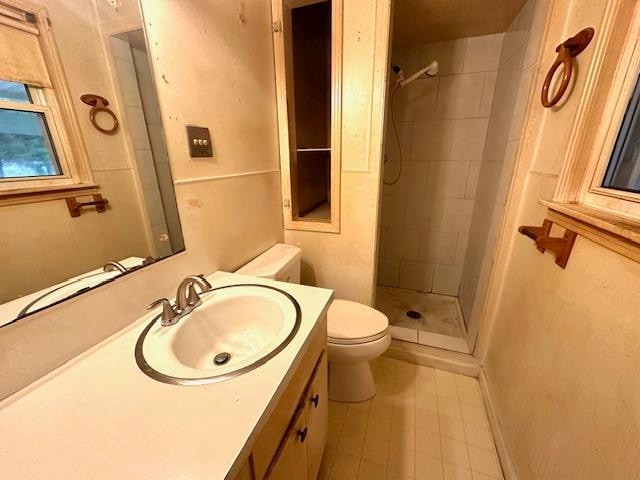 bathroom with vanity, a tile shower, toilet, and tile patterned flooring