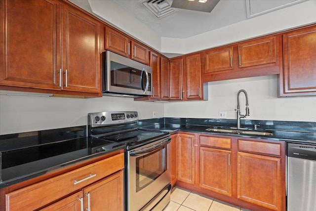 kitchen featuring dark stone countertops, light tile patterned floors, appliances with stainless steel finishes, and sink