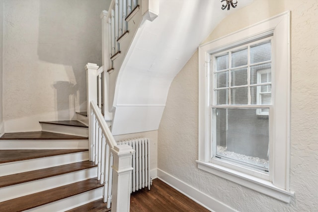 stairs featuring lofted ceiling, radiator heating unit, and hardwood / wood-style flooring