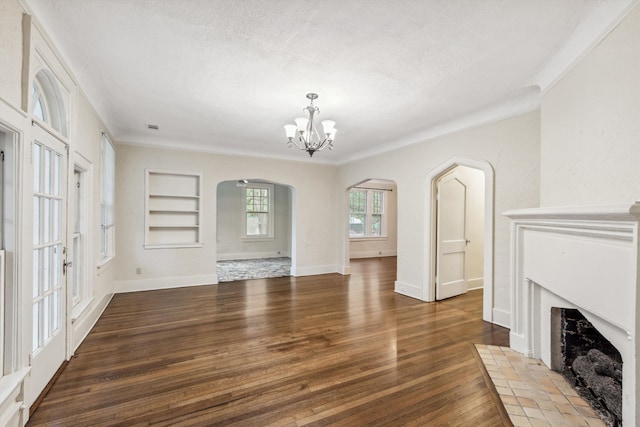 unfurnished living room featuring a textured ceiling, a chandelier, dark wood-type flooring, a fireplace, and built in shelves