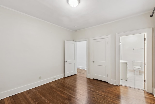 unfurnished bedroom with a closet, ensuite bathroom, ornamental molding, and dark hardwood / wood-style floors