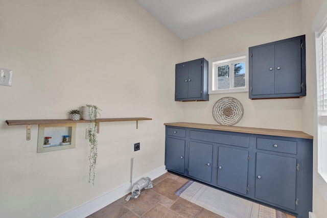 clothes washing area with stone finish flooring, electric dryer hookup, cabinet space, washer hookup, and baseboards