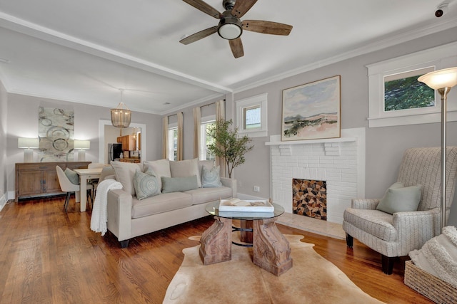 living room featuring a ceiling fan, baseboards, a brick fireplace, crown molding, and wood finished floors