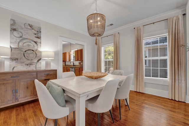 dining room with an inviting chandelier, ornamental molding, visible vents, and wood finished floors