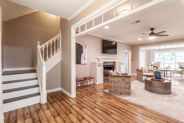 living room featuring ornamental molding, a fireplace, wood-type flooring, and ceiling fan