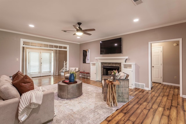 living room with hardwood / wood-style floors, a tiled fireplace, crown molding, and ceiling fan