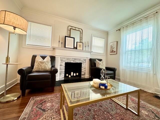 sitting room with a stone fireplace, ornamental molding, and dark hardwood / wood-style flooring