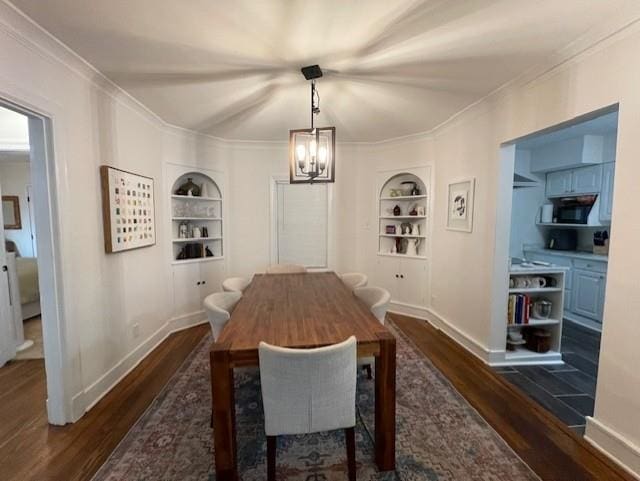 dining space featuring crown molding, built in shelves, an inviting chandelier, and dark hardwood / wood-style flooring