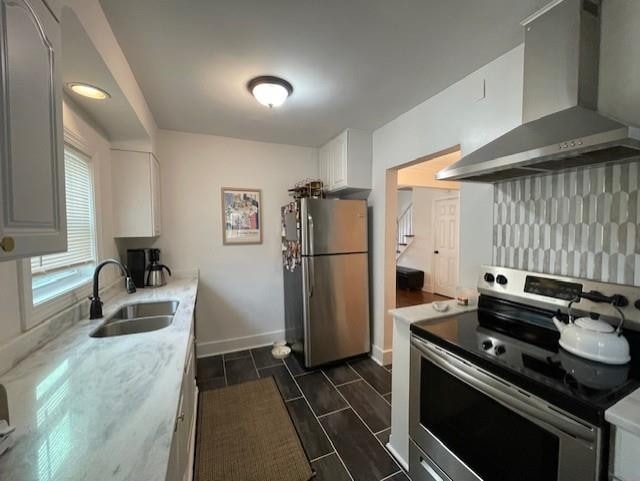 kitchen with wall chimney range hood, white cabinets, tasteful backsplash, appliances with stainless steel finishes, and sink