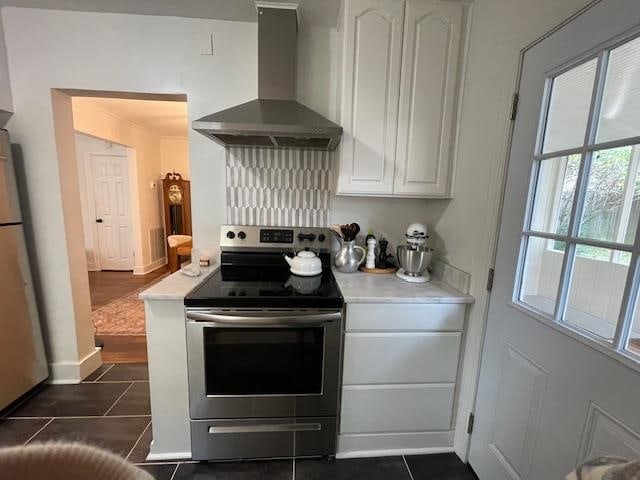 kitchen featuring white cabinets, backsplash, appliances with stainless steel finishes, dark tile patterned floors, and wall chimney exhaust hood