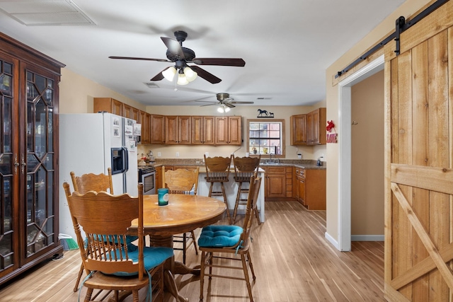 dining area featuring light hardwood / wood-style floors, sink, a barn door, and ceiling fan