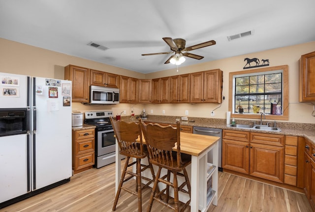 kitchen with appliances with stainless steel finishes, sink, ceiling fan, light stone counters, and light hardwood / wood-style flooring