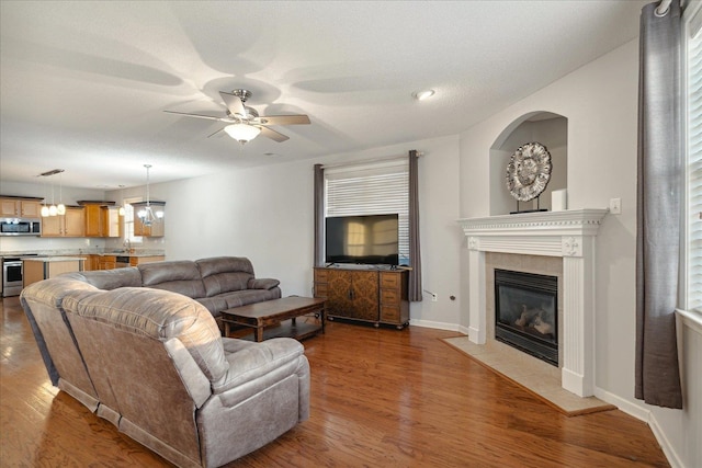 living room featuring dark wood-type flooring, a tiled fireplace, a textured ceiling, and ceiling fan