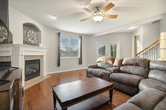 living room with a textured ceiling, ceiling fan, a tiled fireplace, and hardwood / wood-style flooring