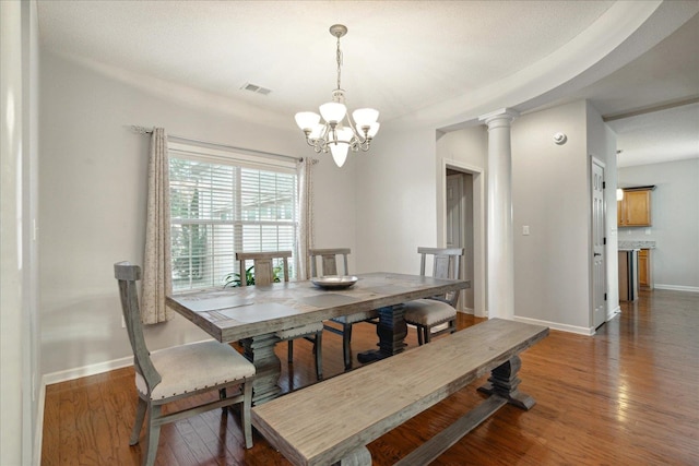 dining space featuring dark wood-type flooring, ornate columns, and a chandelier