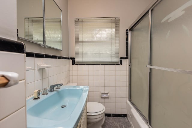 full bathroom featuring vanity, toilet, combined bath / shower with glass door, and tile walls