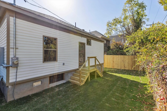rear view of house with fence, a shingled roof, and a lawn