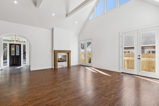 unfurnished living room with french doors, high vaulted ceiling, an inviting chandelier, a wealth of natural light, and arched walkways