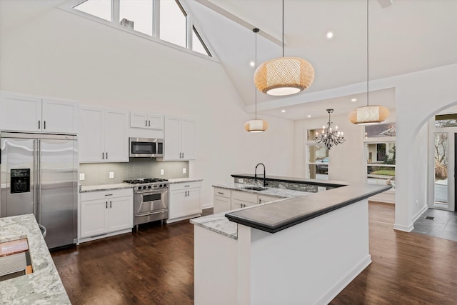 kitchen featuring high vaulted ceiling, high end appliances, a sink, arched walkways, and decorative backsplash