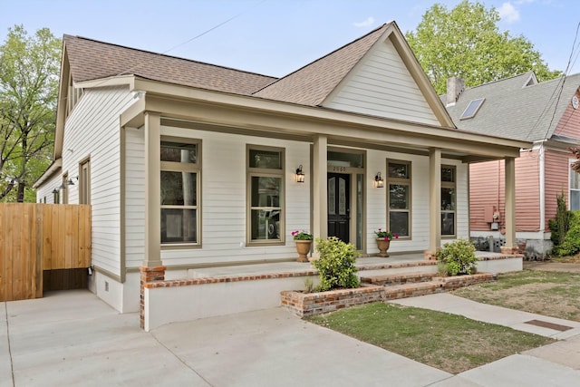 view of front facade with a porch, fence, and a shingled roof