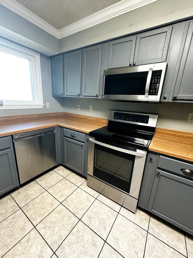 kitchen featuring appliances with stainless steel finishes, wood counters, a textured ceiling, crown molding, and light tile patterned floors