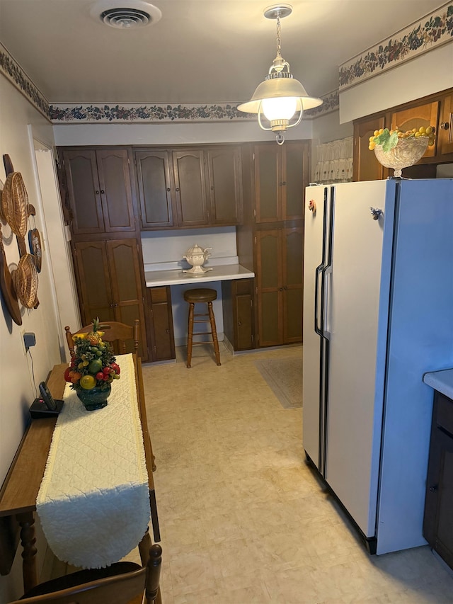 kitchen featuring dark brown cabinetry, white refrigerator, and hanging light fixtures