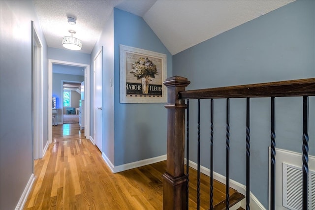 hallway with a textured ceiling, light wood-type flooring, and vaulted ceiling