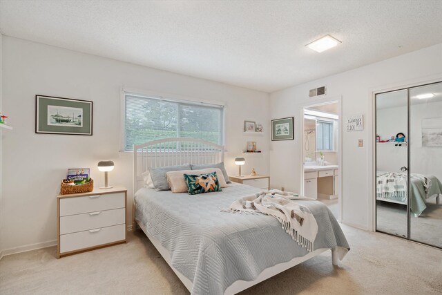 bedroom with a closet, a textured ceiling, light colored carpet, and ensuite bathroom