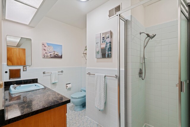 bathroom featuring tile walls, a shower with door, vanity, toilet, and a skylight