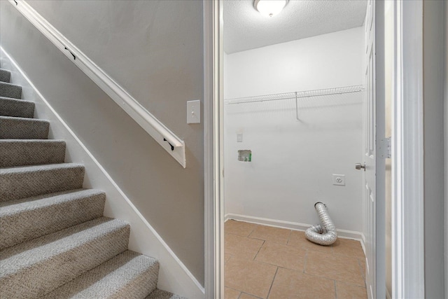 washroom with electric dryer hookup, a textured ceiling, and light tile patterned floors