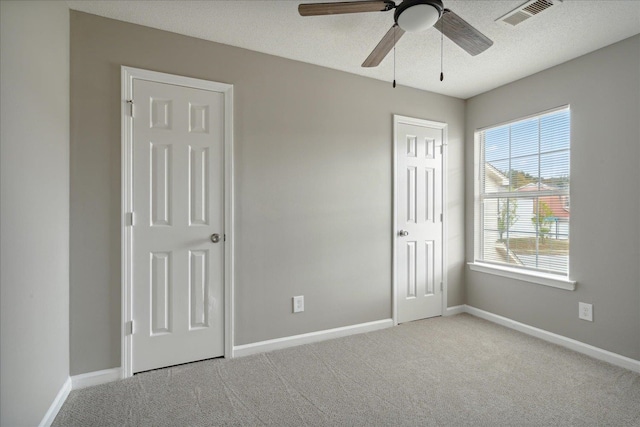 unfurnished bedroom with ceiling fan, light carpet, a textured ceiling, and multiple windows