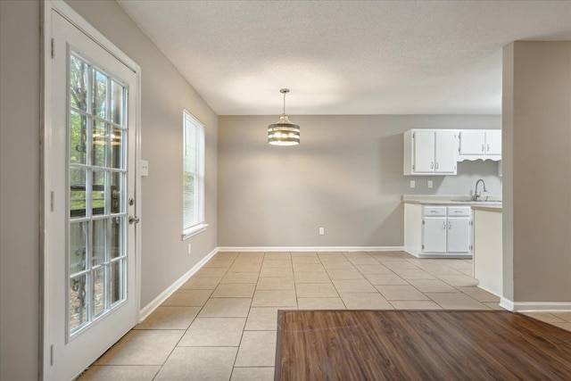 kitchen with sink, pendant lighting, light wood-type flooring, white cabinets, and a textured ceiling