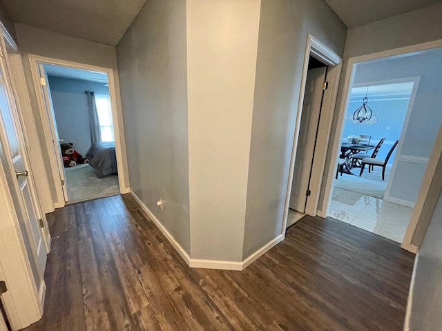 corridor with dark wood-type flooring and an inviting chandelier