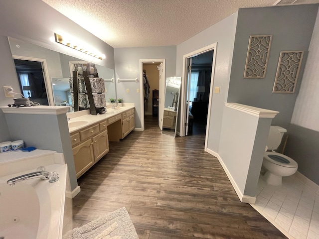 bathroom with wood-type flooring, vanity, a textured ceiling, toilet, and a tub to relax in