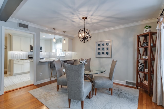 dining space with sink, a notable chandelier, ornamental molding, and light hardwood / wood-style flooring