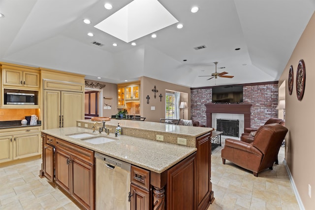 kitchen featuring an island with sink, stainless steel appliances, sink, light stone counters, and a fireplace