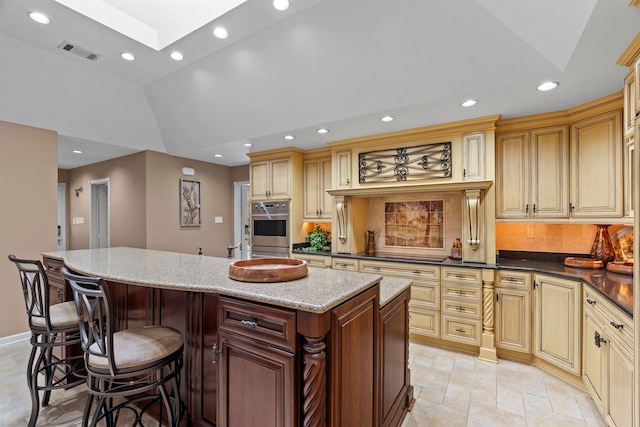 kitchen with a center island, double oven, stovetop, dark stone countertops, and lofted ceiling with skylight