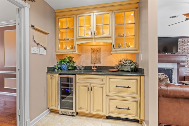 bar with sink, a brick fireplace, dark stone counters, wine cooler, and decorative backsplash