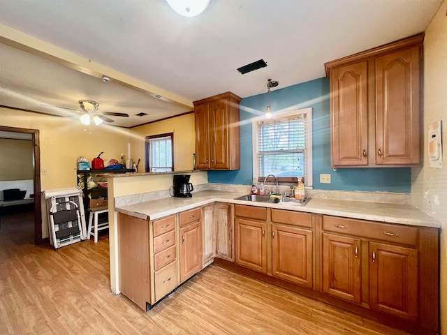 kitchen with sink, kitchen peninsula, decorative light fixtures, and light wood-type flooring