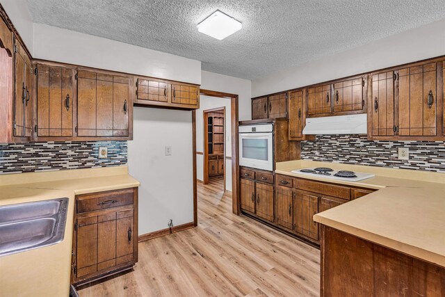 9430 Monasco Rd, Millington, TN 38053 - kitchen featuring white appliances, under cabinet range hood, light wood-style flooring, a textured ceiling, and light countertops