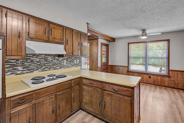 kitchen featuring backsplash, kitchen peninsula, wooden walls, white electric stovetop, and light hardwood / wood-style flooring