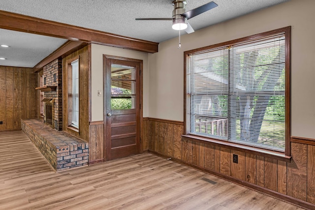 interior space with a fireplace, a textured ceiling, light wood-type flooring, and wood walls