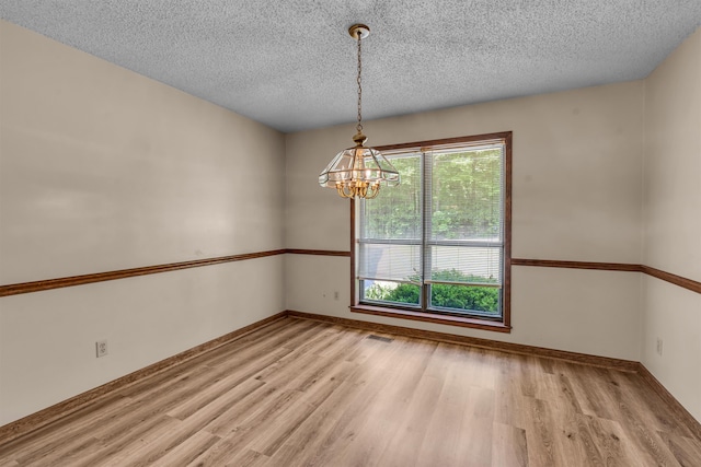 spare room with a textured ceiling, a chandelier, and light wood-type flooring