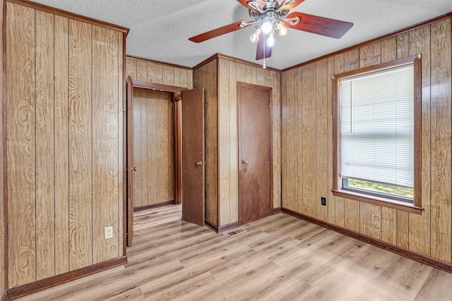 unfurnished bedroom with wooden walls, light hardwood / wood-style flooring, a textured ceiling, and ceiling fan